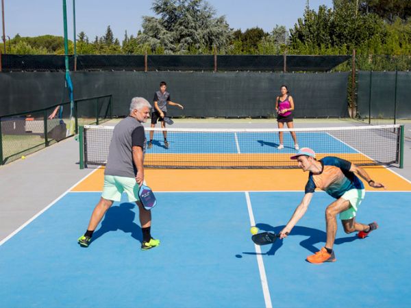 Vận động viên Pickleball thực hiện cú giao bóng dưới tay (Underhand Serve), đảm bảo điểm tiếp xúc dưới thắt lưng và paddle hướng xuống, tuân thủ luật chơi Pickleball.